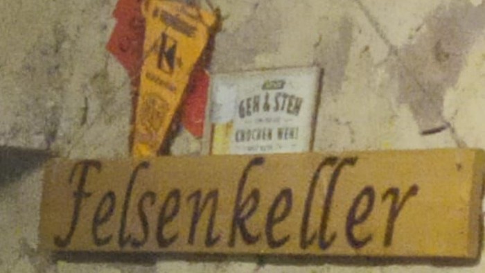Ein rustikales Steinschild mit der Aufschrift „Felsenkeller“ ist mit bierbezogenen Dekorationen und einer nahen Speisekarte versehen.
