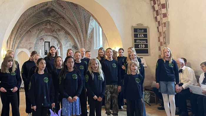 En gruppe af skolebørn og lærere samlet i en historisk hal.