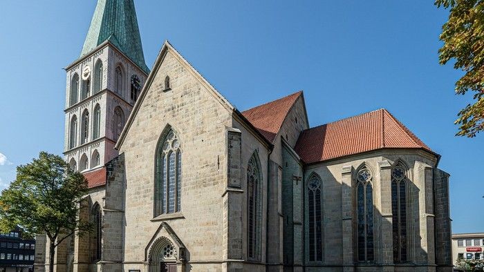 Historische Kirche mit gotischer Architektur, hohem Turm, steinerner Fassade und großen Buntglasfenstern.