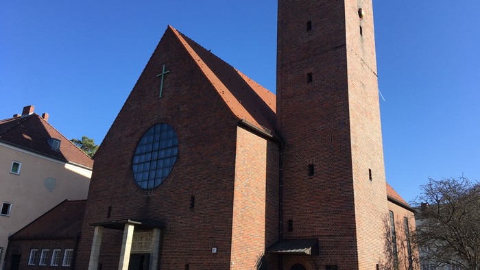 Die Kirche hat einen hohen Turm mit Uhr und ein großes Rundfenster.