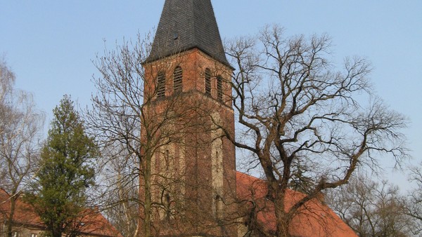 Historische Steinkirche mit hohem Backsteinturm und steilem Satteldach, umgeben von kahlen B�umen.
