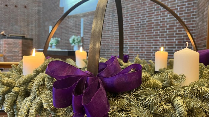 En festligt pyntet bord med grønne blomster, lysstaker og en stor violet farvet bue.