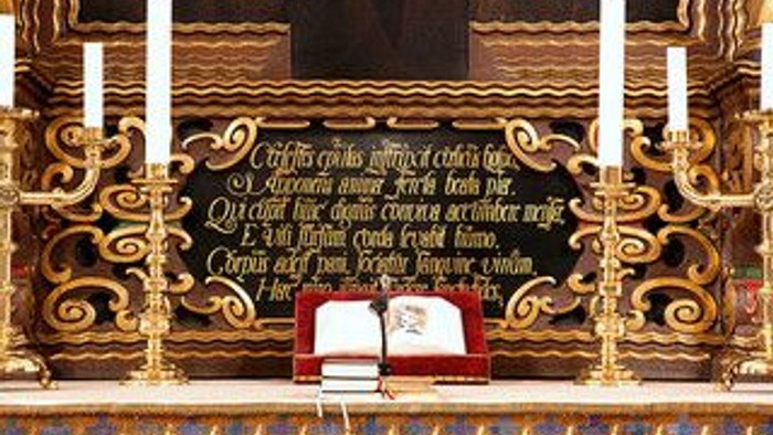 Elegant alter med udsmykkede gyldne udskæringer, lys og en åben bog med religiøs tekst.