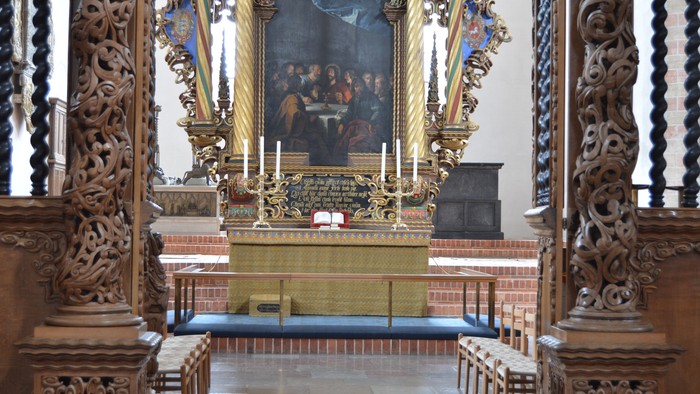 Udskåret kirkealter prydet med detaljerede træskærerier, gyldne detaljer og et indrammet religiøst maleri ovenover.