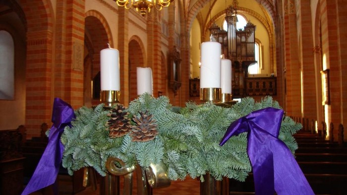 Elegant kirkealter pyntet med stedsegrønne krans, lys, kogler og lilla bånd i en festlig sæson.