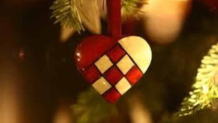 Et festligt hjerteformet julepynt med røde og hvide geometriske mønstre hænger på et pyntet juletræ.