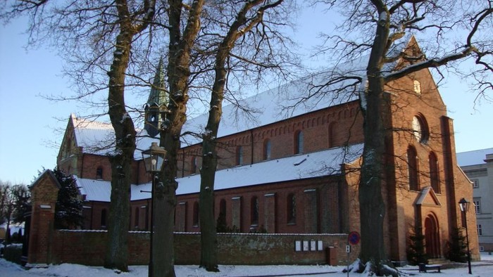 En sneklædt murstenskirke omgivet af nøgne træer på en stille vintergade.