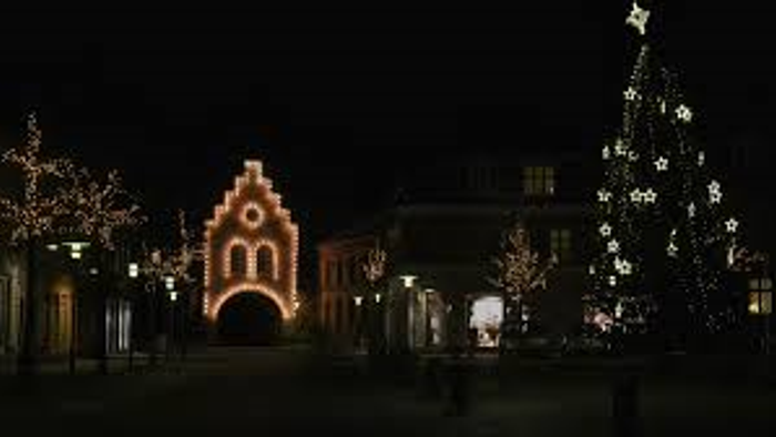 En festlig nattescene med oplyste bygninger, et stort pyntet juletræ og blinkende julelys.