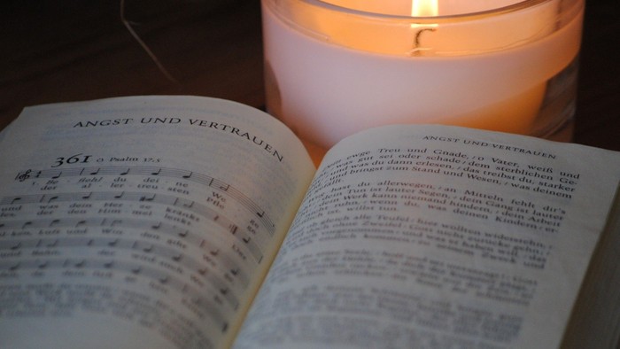 Öffne das Gesangbuch mit dem Titel *„Angst und Vertrauen“* und stelle eine brennende Kerze daneben, um eine ruhige Atmosphäre zu schaffen.
