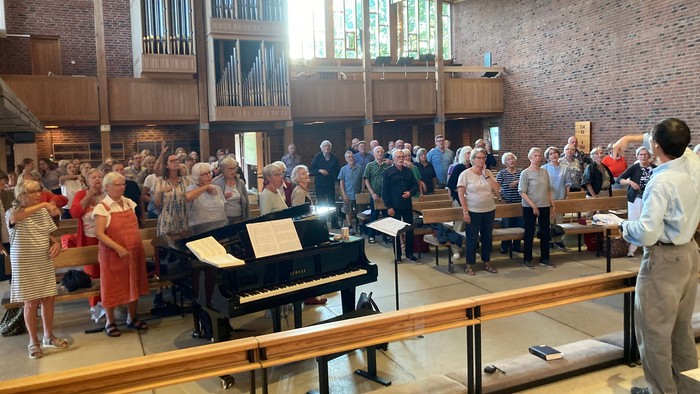 En gruppe øver musik i en kirke med orgel og klaver, ledet af en dirigent.