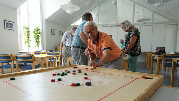 En gruppe ældre folk spiller carrom i et lys og rummeligt rum