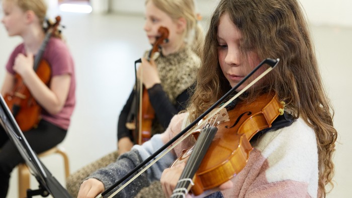 Tre unge piger spiller violin i en klassesal.