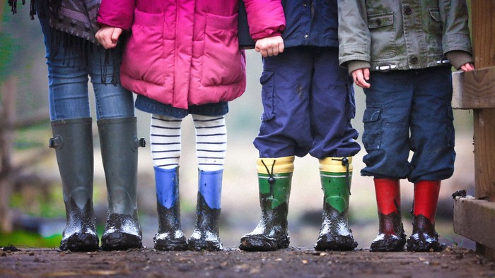 Kinder, die Gummistiefel tragen und im Matsch stehen.