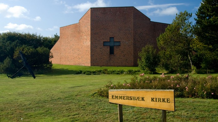 En rød murstenskirke med et blå kors på fasaden og et skilt der siger 