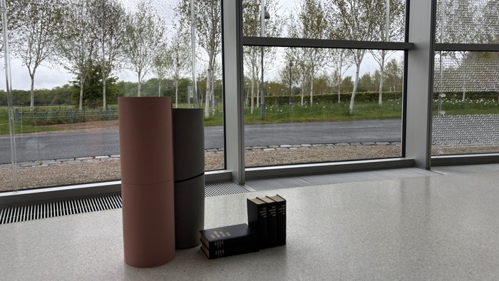 Moderne indendørs rum med cylindriske siddepladser, store vinduer og udendørs træer synlige gennem glasset.