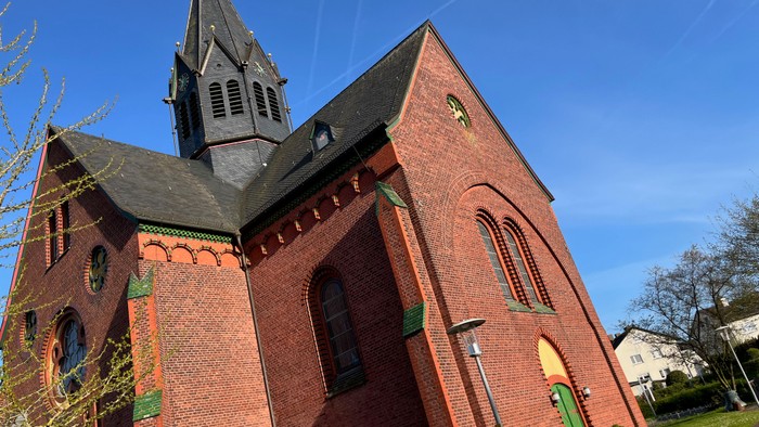 Eine charmante Backsteinkirche mit hohem Turm und Bogenfenstern unter einem klaren blauen Himmel.