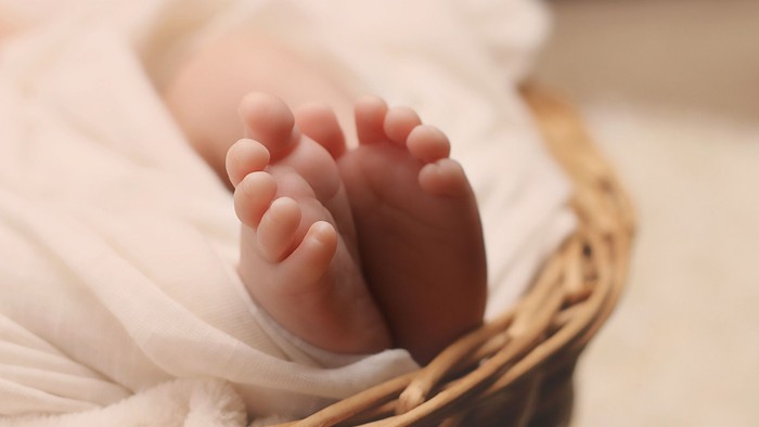 Et nærbillede af en babys små fødder, forsigtigt indsvøbt i en hvid klud inde i en vævet kurv.