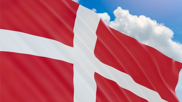 Dansk flag waver i vinden mod et blåt himmel.