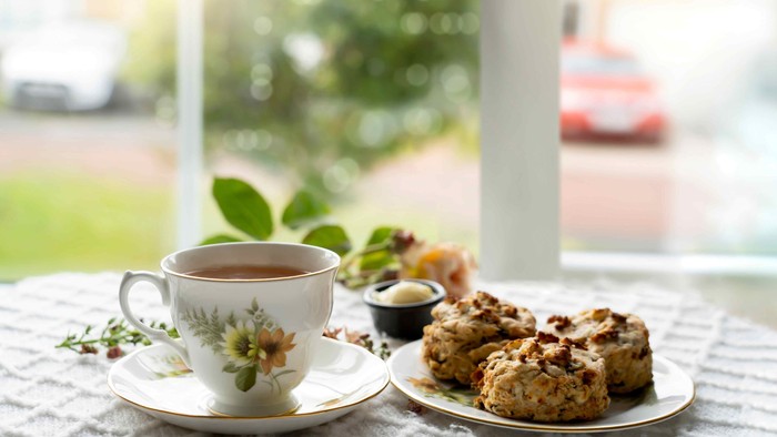 Eine gemütliche Szene mit einer blumigen Tasse Tee, herzhaften Scones und einer ruhigen Aussicht nach draußen durch ein Fenster.