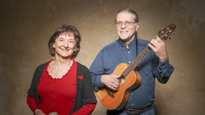Ein lächelndes Paar, einer hält eine Gitarre und der andere einen kleinen Ball, posiert fröhlich zusammen.