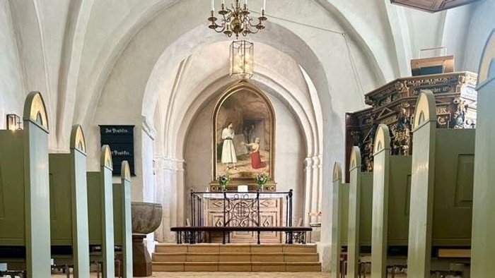 Et roligt kirkeinteriør med træbænke, hvælvede lofter og et centralt alter med religiøs kunst.
