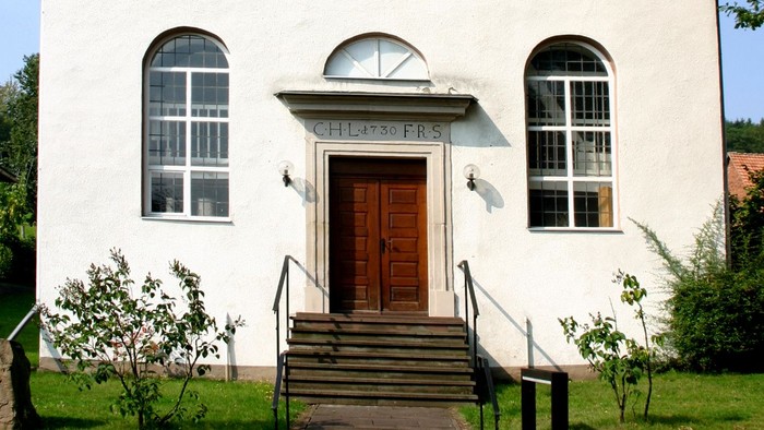 Außenansicht der evangelischen Kirche in Gottstreu. Weiß verputztes Kirchgebäude mit schieferverkleidetem Dachreiter.