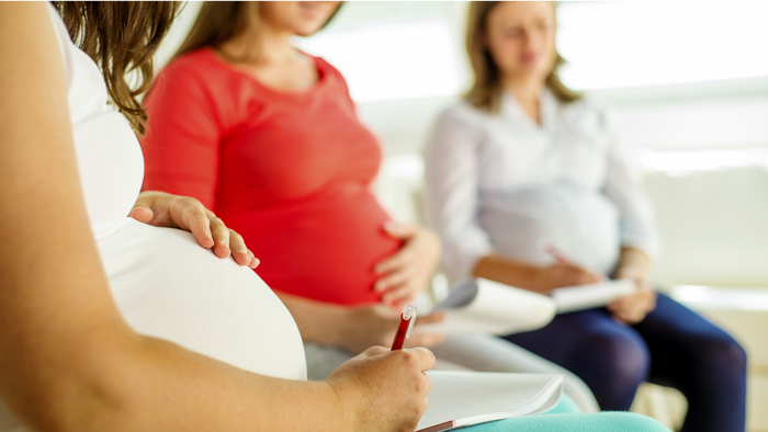 Schwangere Frauen, die an einem Unterstützungsgruppentreffen teilnehmen, sich Notizen teilen und gemeinsam diskutieren.
