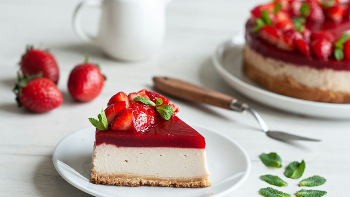 Leckeres Erdbeer-Käsekuchenstück mit frischen Beeren und Minz-Garnitur auf einem weißen Teller.