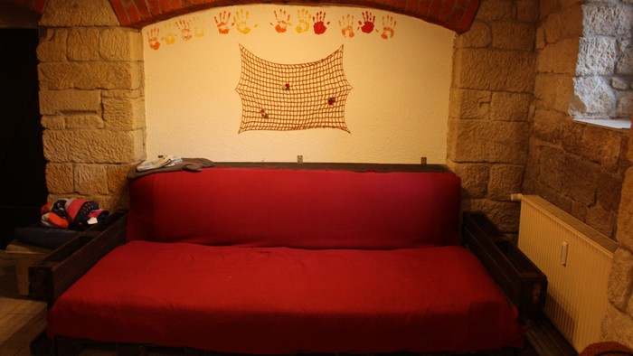 Gemütliches rustikales Zimmer mit rotem Sofa, gemauertem Kamin und Handabdruck-Wandkunst über einer Fischernetz-Dekoration.