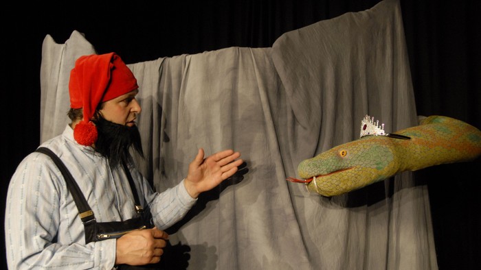 Das Bild zeigt eine Theaterbühne mit einem Zwerg und einer Schlange.
