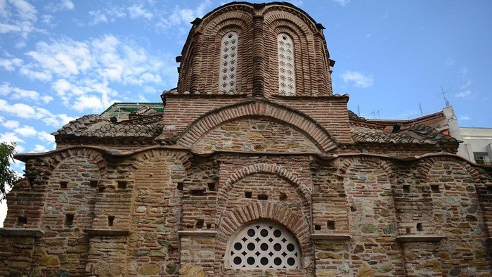 Historisk stenkirke med byzantinske arkitekturelementer og buede vinduer under en klar himmel.
