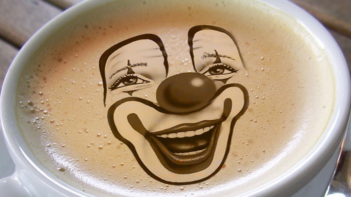Ein fröhliches Clown-Gesicht als Latte Art auf dampfendem Kaffee in einer weißen Tasse.