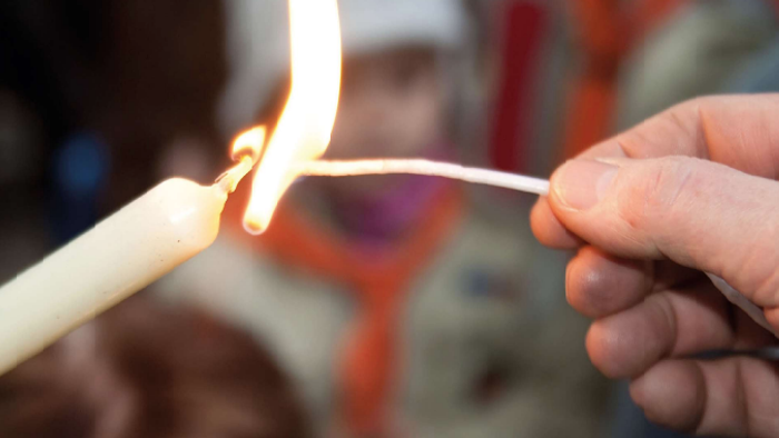 Eine Person zündet eine weiße Kerze mit einem Feuerzeug an.