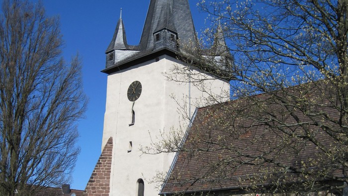 Außenansicht der evangelischen Kirche in Dörnberg. Helles Kirchenschiff aus Naturstein mit rotem Dach und hohem Turm.