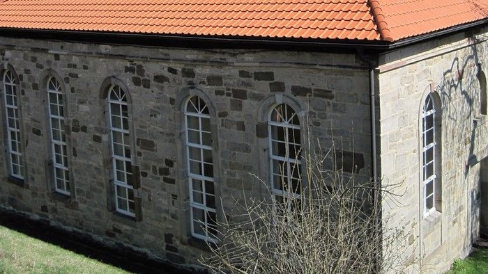 Außenansicht der evangelischen Kirche in Burghasungen. Natursteingebäude mit roten Ziegeldächern und schieferverkleidetem Dachreiter.