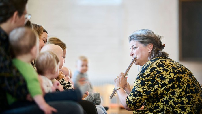 En kvinde i mønstrede jakke taler i et mikrofon til en forsamling.