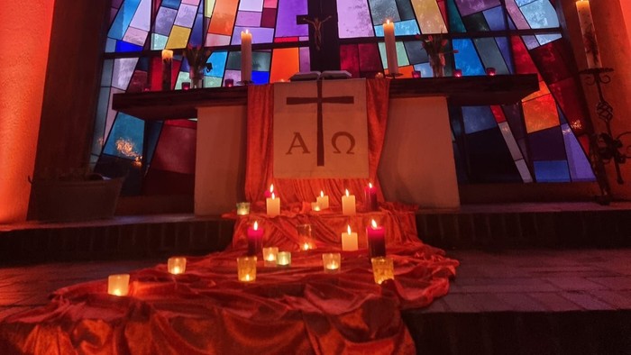 Buntes Glasfenster erleuchtet den mit Kerzen und einem Kreuzsymbol geschmückten Altar.