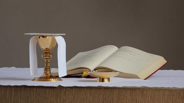 Goldener Kelch und offenes Buch auf weißem Tuch