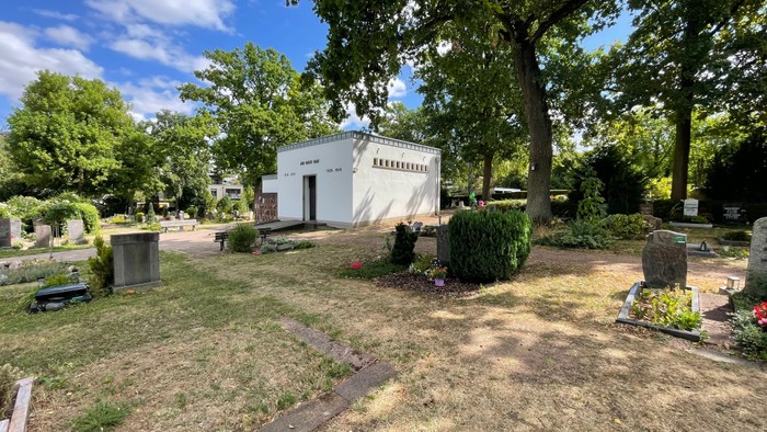 Friedhof mit Bäumen und kleinem Gebäude.