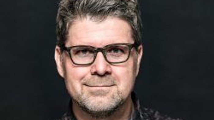 Mann mit Brille und Bart, der ein gemustertes Hemd trägt.