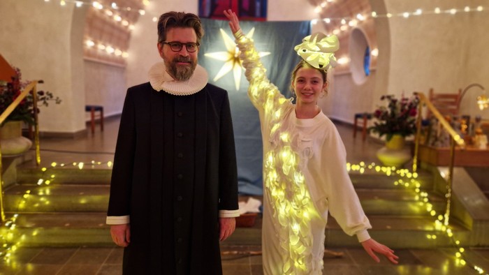 En mand og en kvinde poser i festligt tøj midt i lyskæder og julepynt.
