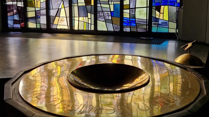 Taufbecken in der Stephanus-Kirche vor buntem Bleiglasfenster