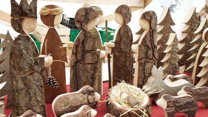 Künstlerisch arrangierte, handgeschnitzte Holzfiguren und Tiere einer Weihnachtskrippe auf einer roten Auslage.