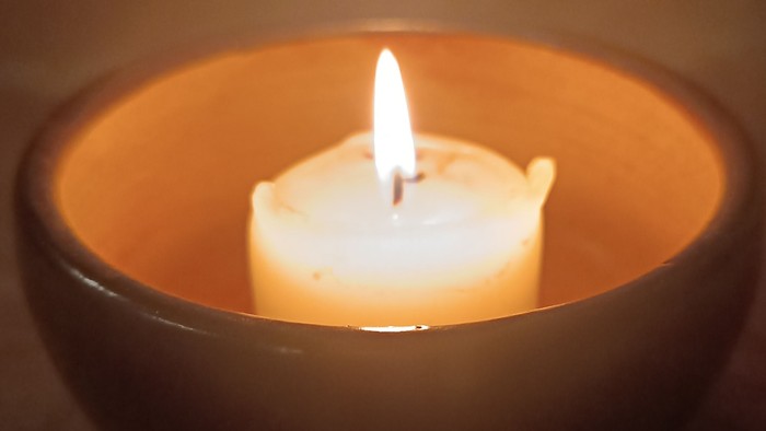 Eine brennende Kerze in einer dunklen, warmtönigen Schale, die sanftes, mildes Licht wirft.