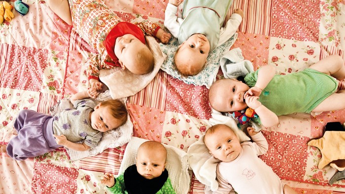 En gruppe babyer klædt i farverige dragter, der ligger sammen på et blomstret tæppe.