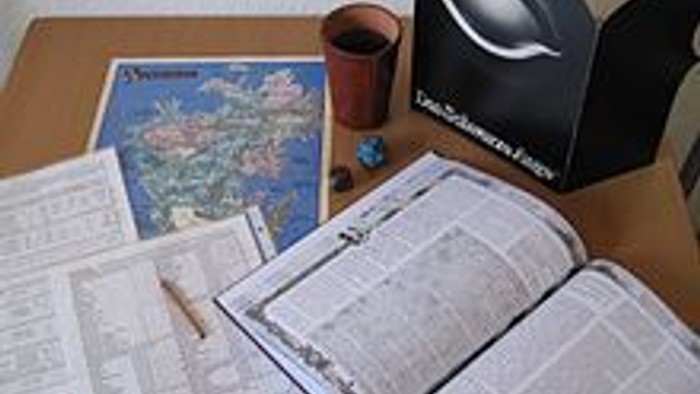 Überladener Schreibtisch mit offener Zeitung, Karte, Stiften und einem Lautsprecher neben einer Tasse.