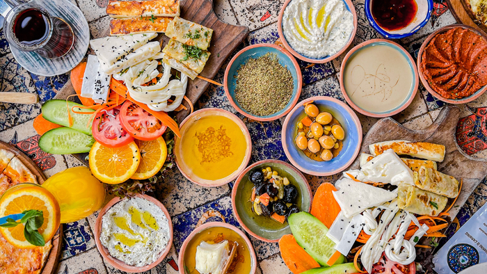 Bunte orientalische Mezze-Auswahl mit verschiedenen Dips, Broten, Mezes und frischem Gemüse auf einem gemusterten Tisch.