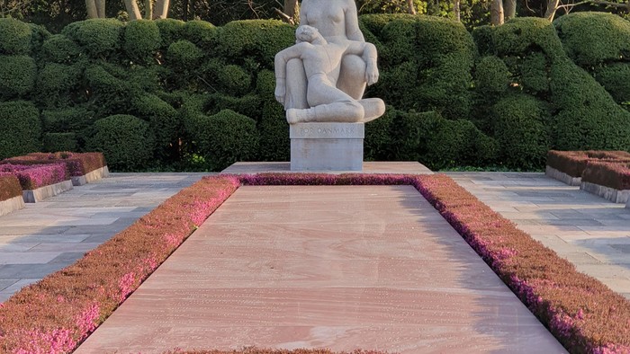 Rolig havekunst af siddende figur omgivet af anlagt beplantning og et rektangulært vandbassin.