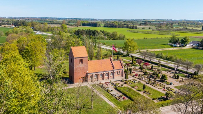En stor rød murstenskirke i grønne landskab med vej og skov i nærheden