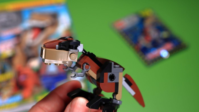 Eine Hand hält eine kleine LEGO-Roboterfigur mit Anleitungen im Hintergrund.